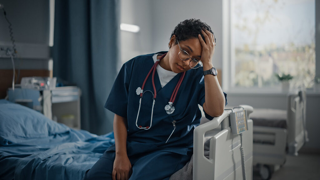 A burned out locum physician sitting on a hospital bed with a frustrated expression