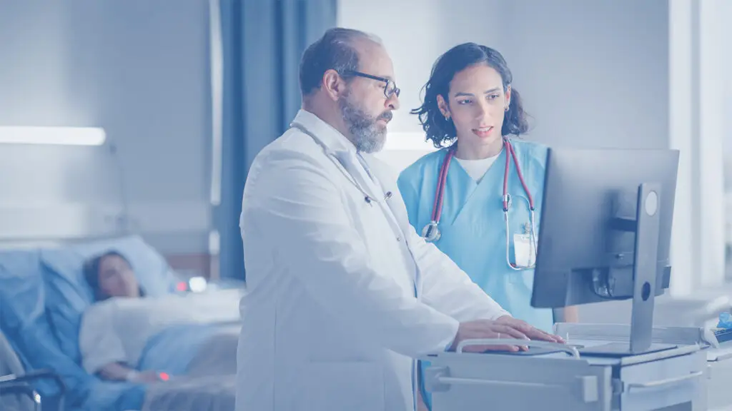 A locums gastroenterologist standing in front of a computer with another physician.