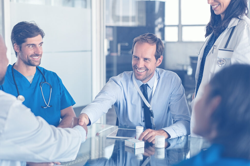 A recruiter shaking hands with a healthcare professional, surrounded by other medical staff.